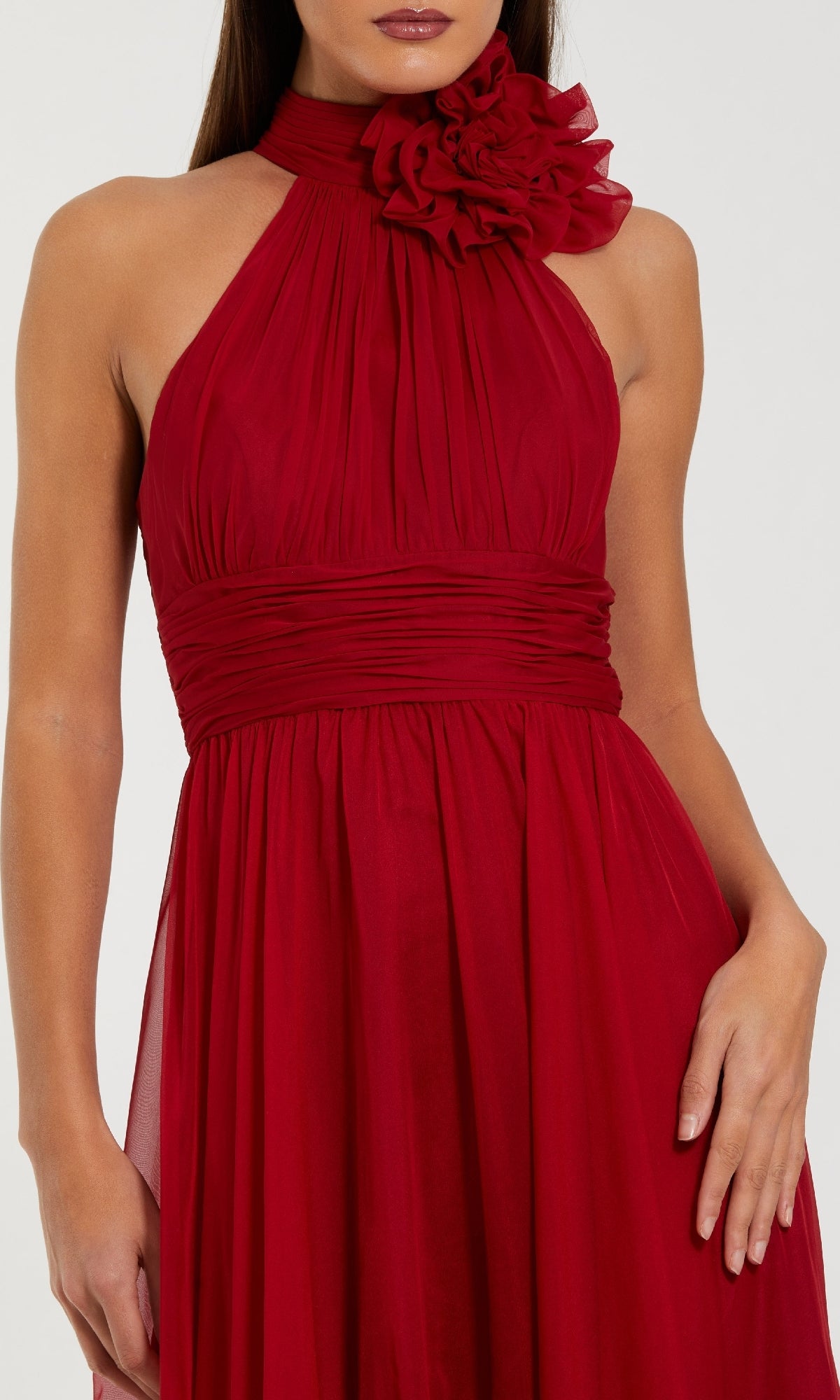 Woman in the Mac Duggal 56254 long formal dress: a sleeveless, dark red chiffon gown with a halter neckline, ruched bodice, and bold fabric flower accent at the neck.